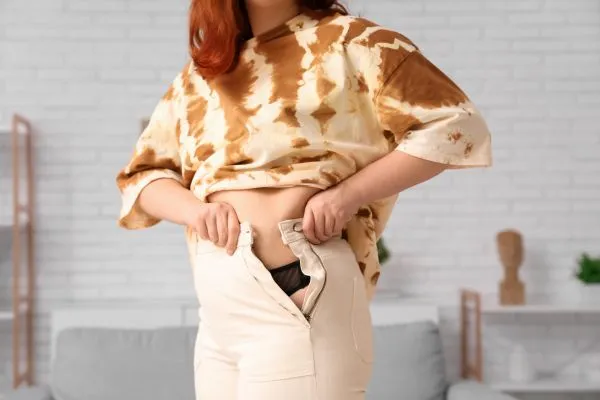 Image of woman trying to do her trousers up after pregnancy weight gain Highworth