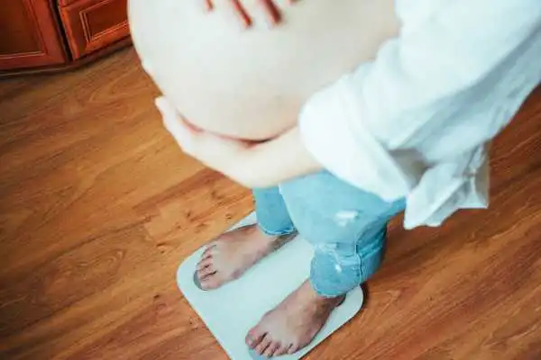 Image of woman weighing herself and experiencing weight gain through pregnancy Highworth